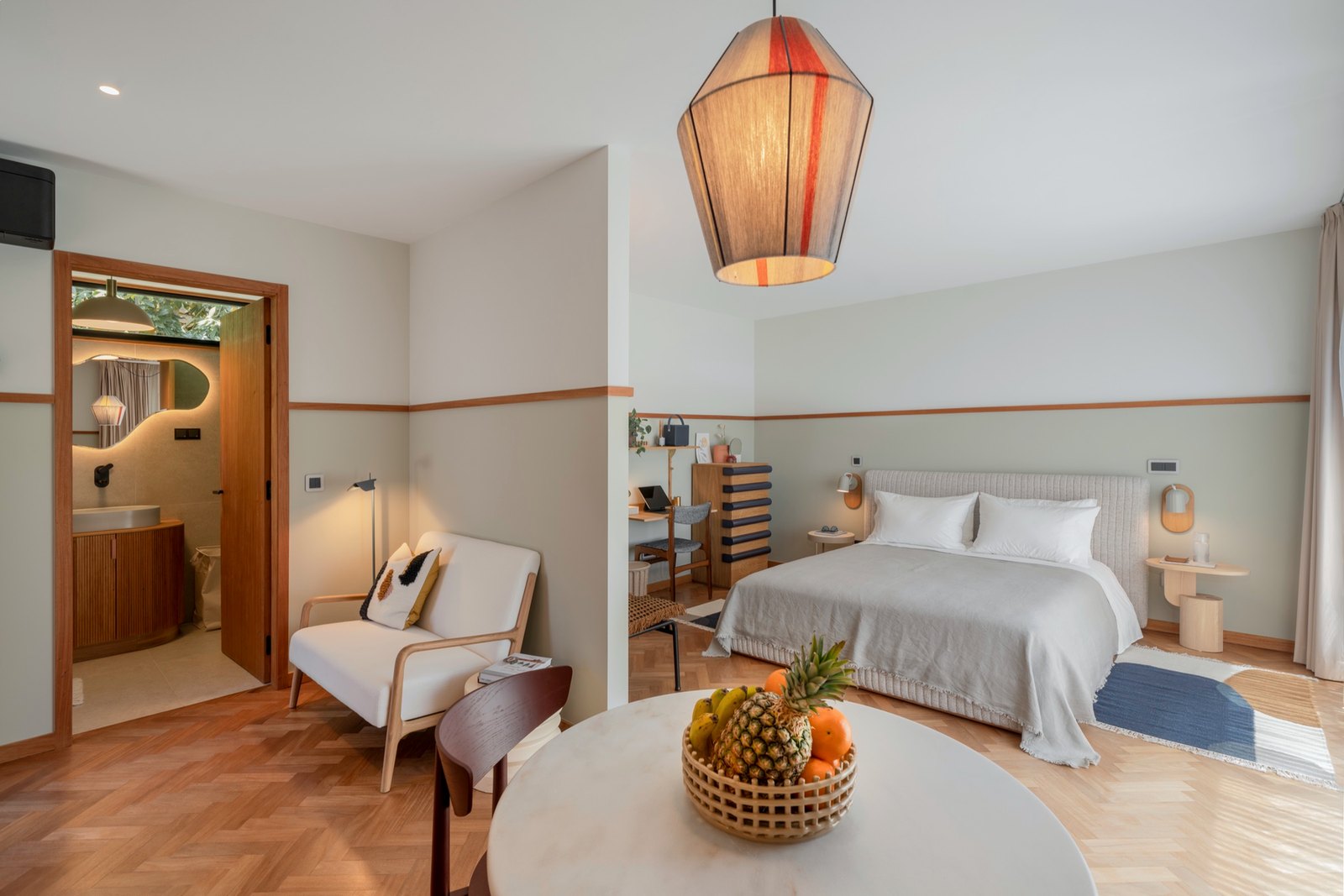 Botânica Living — Bedroom with a striped pendant light, an armchair and a round marble table with a fruit bowl