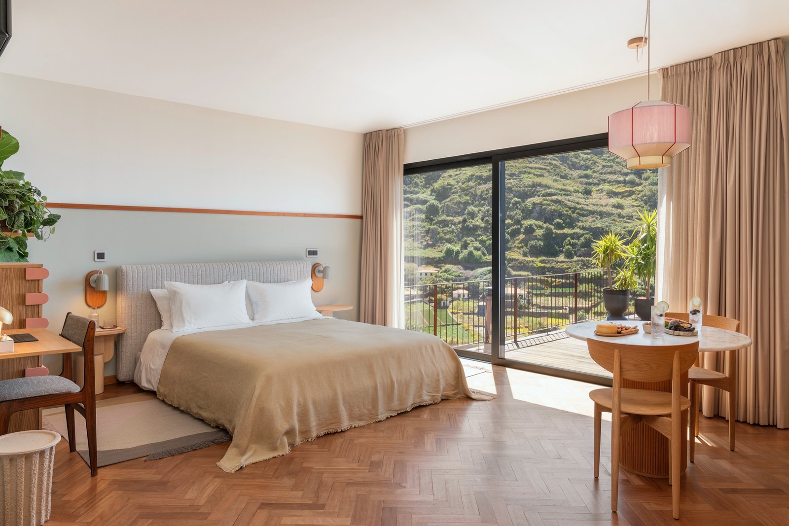 Botânica Living — Bedroom with a linen bedspread and a glass wall opening onto a balcony and the terraced hillside
