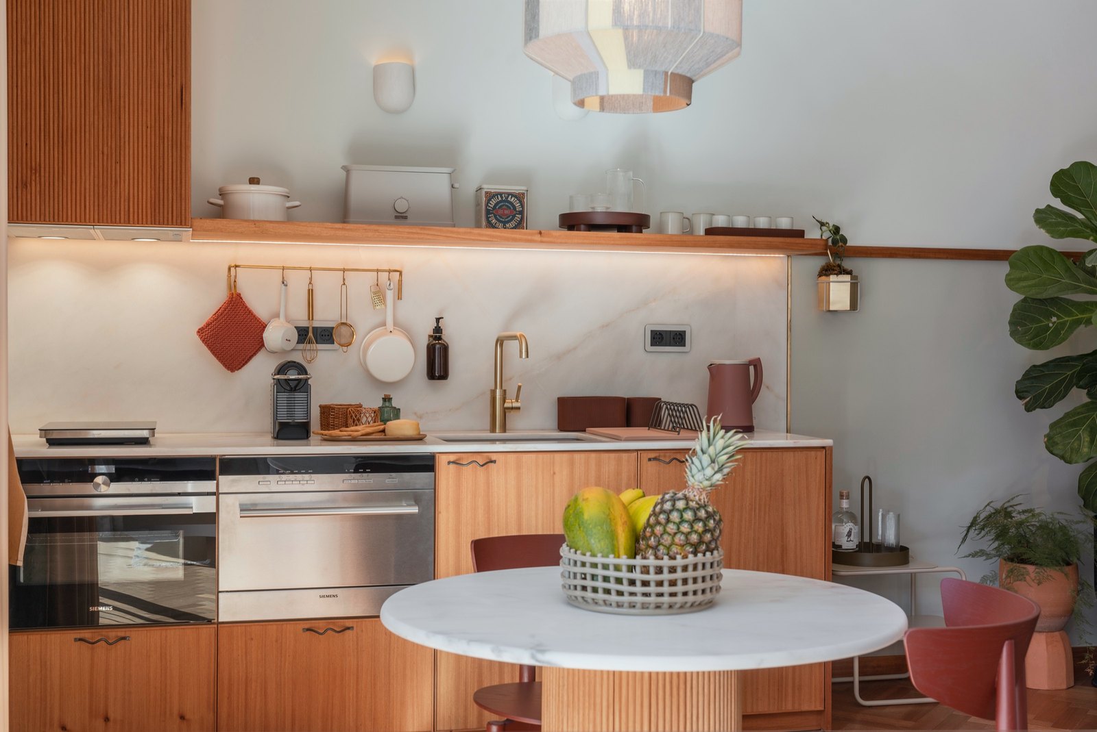 Botânica Living — Kitchen with timber units, a marble splashback and a round table under a woven pendant