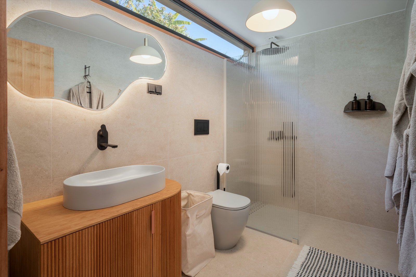 Botânica Living — Bathroom with an organic-shaped mirror, a stone basin on a fluted timber vanity and a glass shower