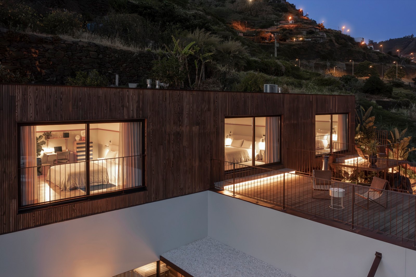 Botânica Living — The timber-clad house at dusk, with the rooms lit behind large windows