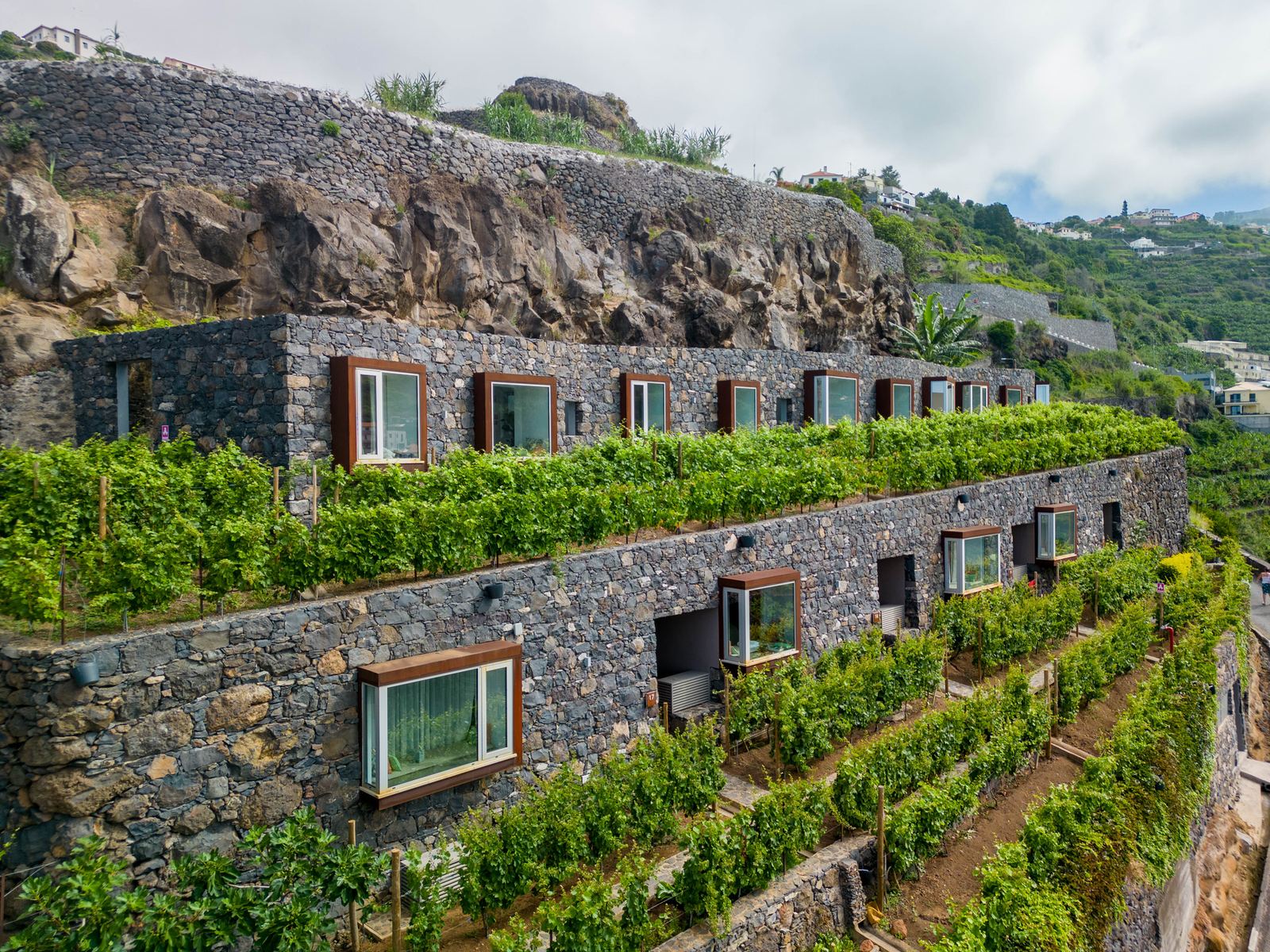 Socalco Nature Calheta — The stone building set into terraced vineyards on the hillside, seen from above