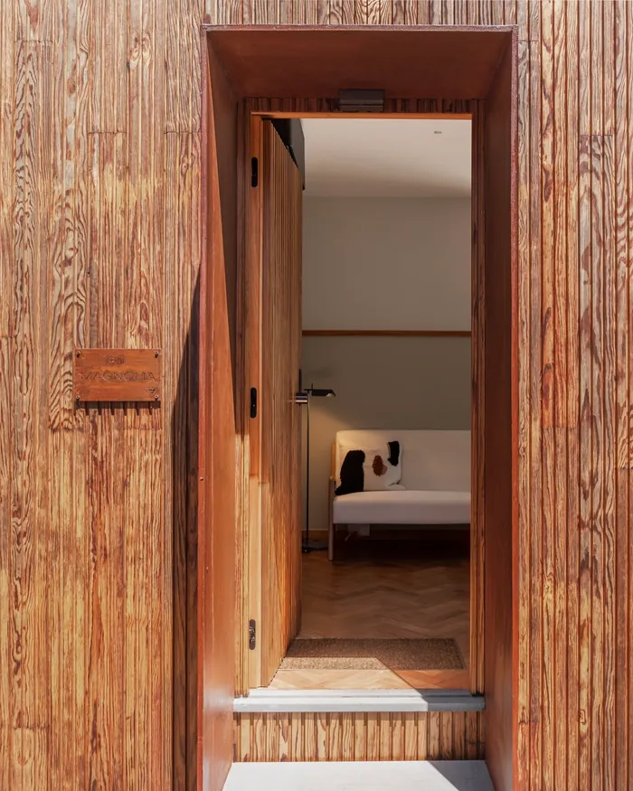 Vertical timber boards around a doorway, with a bedroom visible through the opening, at Botânica Living